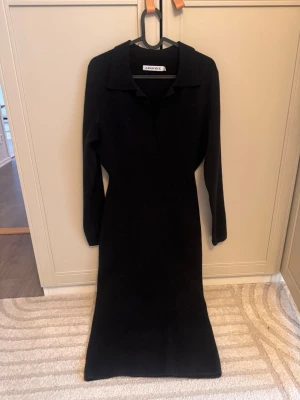 Svart långärmad stickad klänning Adoore - Säljer en svart långärmad klänning från Adoore. Klänningen har krage och v-ringad öppning framtill, är figurnära och går ner till vaden. Perfekt för dig som gillar stilrena och klassiska plagg.