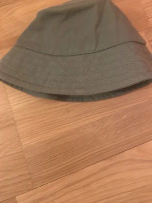 Olivgrön ”fiskar hatt” från Lindex - Snygg olivgrön bucket hat från Lindex i mjukt tyg. Klassisk form med bred, nedåtlutande brätte och diskreta sömmar runt om. Perfekt för en avslappnad och trendig look. Tillverkad i bomullsmix för skön känsla.