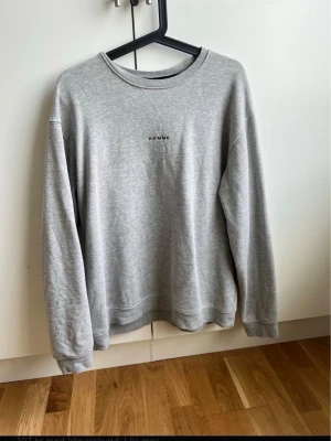 Grå sweatshirt från HOMME - En enkel och stilren grå sweatshirt från HOMME med rund halsringning och diskret svart text på bröstet. Tröjan har långa ärmar och är gjord i mjukt material, perfekt för en avslappnad och trendig stil.
