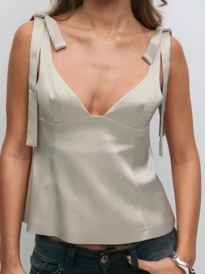 Beige linnetopp med knytband - Stilren beige linnetopp med djup v-ringning och breda axelband som knyts i rosetter på axlarna. Toppen har en lätt utsvängd passform och är tillverkad i ett slätt, satinliknande material. Perfekt för en trendig och enkel look.