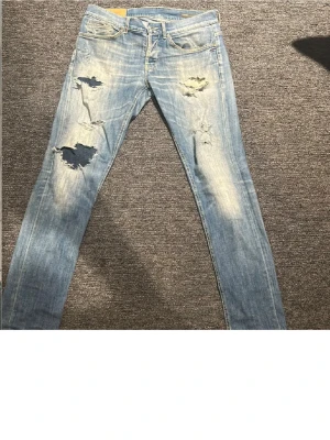 Blå dondup george jeans  - Säljer ett par blå jeans med slitningar på låren och knäna. De har en slim passform och är perfekta för en avslappnad stil. Jeansen har klassisk femficksdesign och stängs med dragkedja och knapp. Modellen är 185. Pris kan diskuteras vid snabb affär!