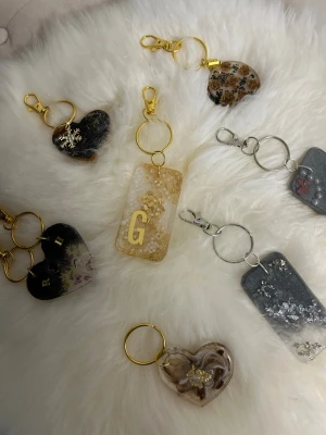 Handgjorda nyckelringar i resin - Unika nyckelringar i resin med inslag av torkade blommor, glitter och bokstäver. Finns i både hjärt- och rektangulär form, med detaljer i guld och silver. Perfekt accessoar till väskan eller nyckelknippan för en personlig touch.