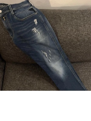 Blå slitna jeans från Replay - Säljer ett par blå jeans från Replay med snygga slitningar och tvättade detaljer. Jeansen har klassisk femficksmodell, normal midja och raka ben. Perfekta för en avslappnad och trendig look. Passar en som är runt 170-175, skräddat dom 