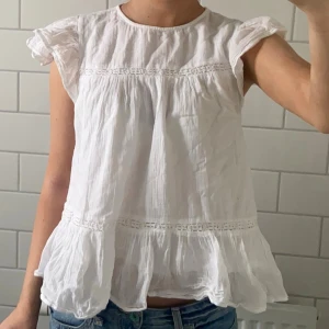 Vit volangblus med spets & volang  - Söt vit blus med volanger från Gina Young. Egentligen storlek 158/164 men skulle säga att den sitter som XS/S! Så fin till sommaren 