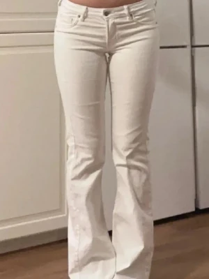Vita bootcut jeans med låg midja - Säljer ett par vita bootcut jeans med låg midja och klassisk femficksmodell. Jeansen har utsvängda ben och stängs med knapp och dragkedja. Perfekta för dig som vill ha en clean och stilren look. 