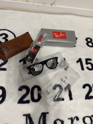 Svarta Ray-Ban Wayfarer solglasögon - Klassiska svarta Ray-Ban Wayfarer solglasögon med blank finish och mörka glas. Snygg tidlös design med Ray-Ban-logga på skalmen. Kommer med originalfodral, putsduk och box. Perfekta för dig som vill ha en ikonisk accessoar till sommaren.