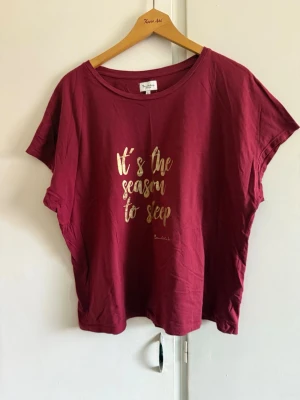 Vinröd pyjamastopp med Bandeld - Mysig vinröd pyjamastopp från Bandelid med korta ärmar och rund halsringning. Framsidan har ett tryck i guld med texten 'It's the season to sleep'. Perfekt för slappa dagar och nätter. Materialet känns mjukt och bekvämt mot huden.