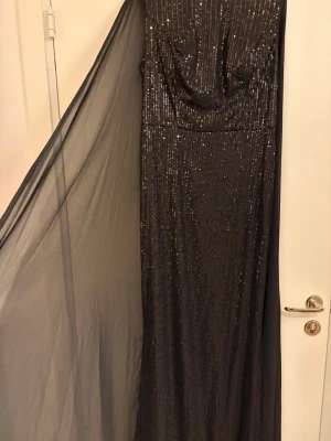 Svart glittrig långklänning - Elegant svart långklänning med glittriga paljettdetaljer och som är lite extra dramatik och glamour. Perfekt för dig som vill sticka ut på bal eller fest. Använd 1 gång