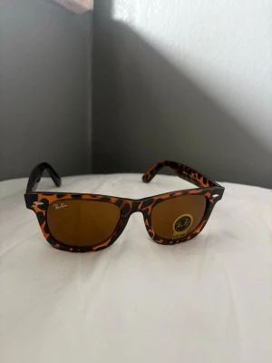 Ray-Ban Wayfarer leopardmönstrade solglasögon - Helt nya och oanvända Ray-Ban Original Wayfarer (RB2140) i klassisk tortoise/sköldpaddsfärg 🤎  • Modell: RB2140 • Original Wayfarer • Hand Made in Italy • 100% UV-skydd • Unisex  Aldrig använda – inga repor, inga märken. En av Ray-Bans mest ikoniska och tidlösa modeller som alltid är trendig.  Perfekta till både vardag och sommar. Säljs då de inte kommit till användning.  Skickas snabbt och säkert