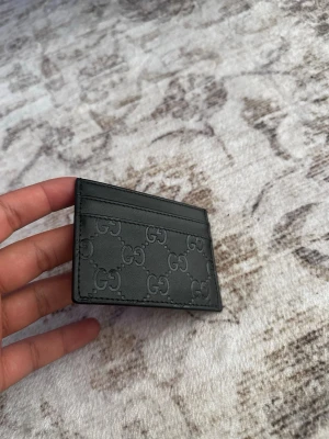 Svart korthållare från Gucci - Snygg svart korthållare från Gucci i läder med präglade GG-loggor över hela ytan. Slimmad och stilren design med flera kortfack både fram och bak. Perfekt för dig som vill ha en exklusiv accessoar i fickan.