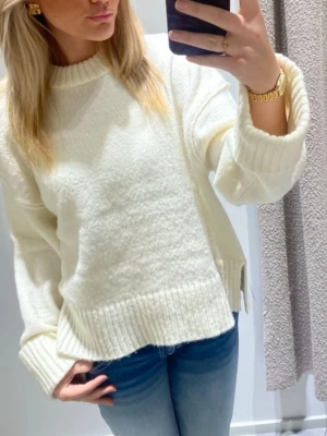 Vit oversized stickad tröja - Säljer en vit oversized stickad tröja med breda ribbade muddar vid ärmslut och nederkant. Tröjan har en rak passform och rund halsringning. Perfekt för dig som gillar en avslappnad och trendig look.