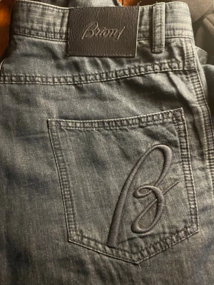 Mörkblå jeans från Brioni - Snygga mörkblå jeans från Brioni med klassisk rak passform. Jeansen har en stor broderad B-logga på bakfickan och en läderpatch med Brioni-märke i midjan. Tillverkade i mjukt denimtyg som ger en exklusiv känsla.