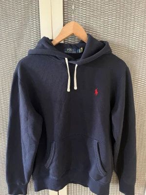 Mörkblå hoodie från Polo Ralph Lauren - Säljer min raffe hoodie då jag inte längre har användning för den. Den är i riktigt bra skick, inga som helst defelekter eller skador, ser nästan helt oanvänd ut, väldigt varsamt använd och är allmänt riktigt fräsch, passar nästan allt och sitter perfekt, storlek S. SKICKA BUD