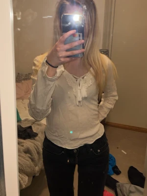 Vit långärmad blus med spets - Söt vit blus med långa ärmar, spetsdetaljer vid halsringningen och knyt framtill. Blusen har en feminin v-ringning och är tillverkad i ett mjukt material som känns skönt mot huden. Perfekt för dig som gillar romantisk stil.