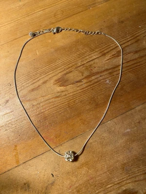 Silverfärgat halsband med glittrande pärla - Säljer ett stilrent silverfärgat halsband med en rund, med diamanter som sitter i en boll. Kedjan är tunn och elegant, och pärlan är dekorerad med små stenar som ger extra bling. Perfekt för dig som gillar enkla men snygga smycken.