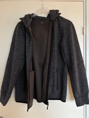 Mörkgrå hoodie med dragkedja - Snygg mörkgrå hoodie från Uniqlo med dragkedja framtill och två sidofickor med dragkedja! Tillverkad i ett mjukt, lite tjockare material med diskret melerad struktur. Huva med dragsko och långa ärmar. Storlek XL men sitter mer som L.