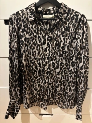 Leopardmönstrad blus från InWear - Snygg leopardmönstrad blus från InWear i svart, grått och vitt. Blusen har lång ärm, klassisk krage och knäppning framtill. Snygga knappar längst ner på armarna. Materialet är glansigt och ger en lyxig känsla. Perfekt för dig som vill sticka ut med ett djurmönster.