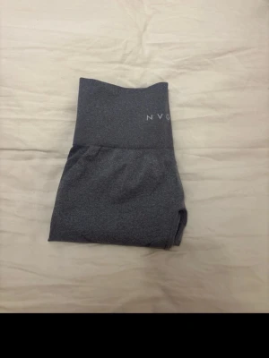 Grå seamless leggings från NVGTN - Säljer ett par grå seamless leggings från NVGTN med hög midja och snygga paneldetaljer längs sidorna. Stretchigt material som sitter skönt och formar sig efter kroppen. Perfekta för gymmet.