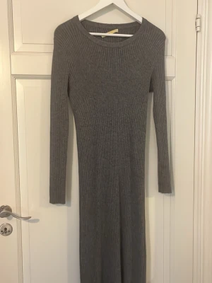 Grå ribbad långärmad klänning - Säljer en lång, ribbad klänning i grått med lång ärm och rund halsringning. Klänningen har en kroppsnära passform och är perfekt för dig som gillar en enkel men stilren look. Materialet känns mjukt och stretchigt, vilket gör den bekväm att bära hela dagen. Har aldrig använt den så den är helt ny fast utan prislapp.💗