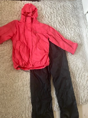 Regnställ  - Säljer ett regnställ med svarta byxor och rosa jacka. Materialet är vindtätt och vattenavvisande och modellen är ganska vanlig.