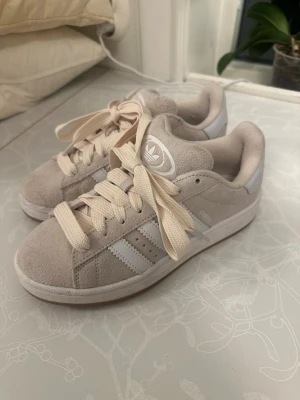 Beige Adidas Campus 00s  - Jag säljer ett par beige adidas campus 00 i storlek 38. Dom är använda ett väldigt fåtal gånger💕
