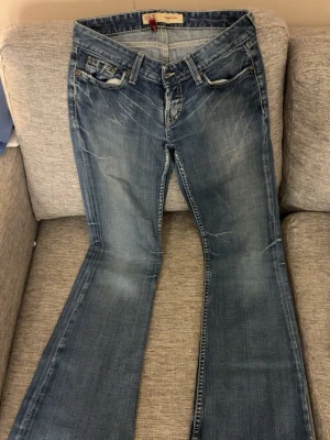 Blå bootcut jeans med snygga ditaljer  - Säljer ett par blå bootcut jeans från Bik Bok, modell Sabrina. Jeansen har slitna detaljer, klassisk femficksdesign och ljus tvätt. Använda några fåtal ggr och känns som nya! skriv om du har funderingar!! hittar inte storleken men är 163 och sitter perfekt i längden! snygga fickor och väldigt lågmidjade 