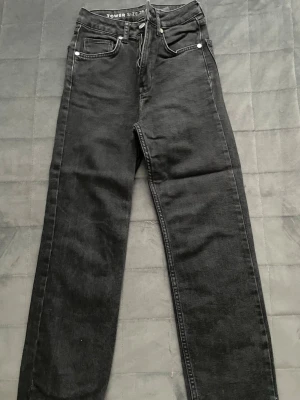 Svarta straight jeans  - Säljer ett par svarta jeans från Bilbok med rak passform och klassisk femficksdesign. Jeansen har hög midja och silverfärgade nitar. Materialet är denim i bomull och de har bälteshällor samt dragkedjegylf.