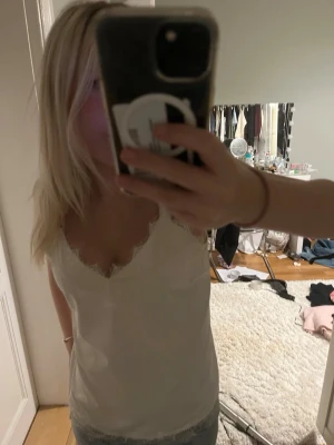 Vit spetskantad linnetopp - Snygg vit linnetopp med spetsdetaljer längs urringningen. Perfekt att styla till jeans eller kjol för en fräsch look. Ärmlös och i mjukt material som känns skönt mot huden.