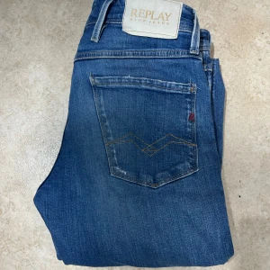Blå jeans från Replay - Säljer ett par blå jeans från Replay med klassisk femficksmodell och snygga slitningar framtill. Jeansen har en rak passform och tydliga sömmar på bakfickan. Perfekta för en avslappnad och trendig look.