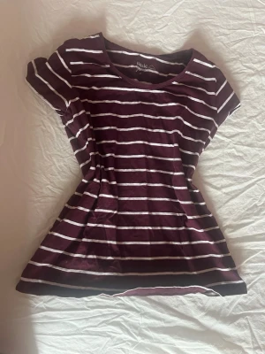 Randig vinröd tröja - Säljer en vinröd topp  med vita horisontella ränder. T-shirten har rund halsringning och korta ärmar. Perfekt för dig som gillar en enkel och avslappnad stil. Materialet är mjukt och känns skönt mot huden. Storlek M men sitter med som S!