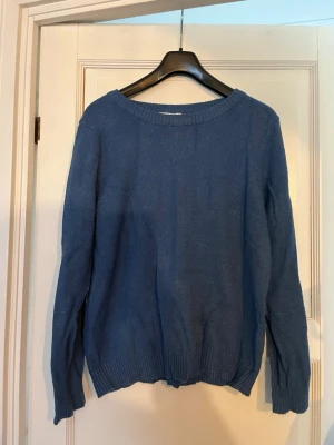 Blå stickad tröja från Vila - Mysig blå stickad tröja från Vila med rund halsringning och ribbade muddar vid ärmslut och nederkant. Perfekt för lager-på-lager och enkel att matcha med jeans eller kjol.