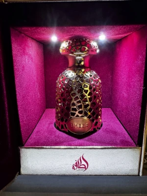 Lyxig parfymflaska Ember i guld - Pris diskuteras. Säljer en exklusiv parfym från Lattafa med namnet Ember. Flaskan har ett unikt guld- och svartmönstrat metallhölje och rundad form. Kommer i en elegant presentbox med lila sammet och gulddetaljer. Perfekt för dig som gillar lyxiga dofter och snygg design.