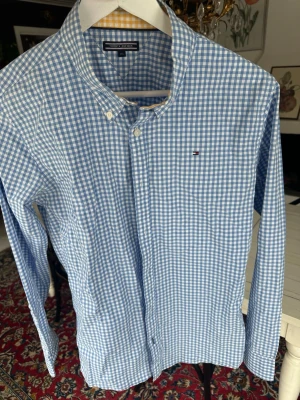 Blårutig skjorta Tommy Hilfiger - Snygg blårutig skjorta från Tommy Hilfiger med klassisk button-down krage och diskret logga på bröstet. Skjortan har långa ärmar, vita knappar och är tillverkad i mjuk bomull. Perfekt för en stilren och avslappnad look.