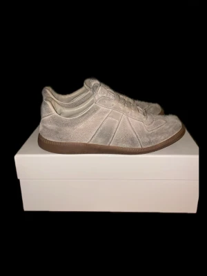 Maison Margiela Replica beige sneakers - Priset kan diskuteras och kan skicka fler bilder Snygga Maison Margiela Replica sneakers i beige mocka med klassisk gummisula. Lågt skaft och stilren design som passar till det mesta. Skorna har vita snören och diskreta detaljer som ger en clean look.
