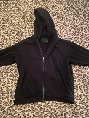 Svart zipup hoodie - En klassisk svart hoodie från Lager 157 med dragkedja framtill och två stora fickor. Hoodien har en rymlig huva och ribbade muddar vid ärmslut och nederkant. Perfekt för en chill och avslappnad stil. Materialet är mjukt och bekvämt, troligtvis bomullsblandning.