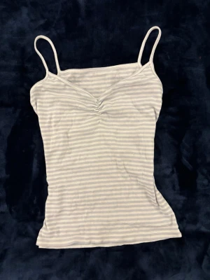Randig vit och blå linnetopp - Säljer en söt randig linnetopp i vitt och ljudblå med tunna axelband och lätt rynkning vid bysten. Perfekt till sommaren och enkel att matcha med jeans eller kjol. Materialet känns mjukt och stretchigt. Köpt i Shanghai i affären W managment.