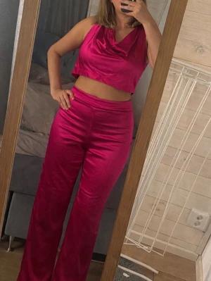 Rosa satin set från Zara - Säljer en snygg rosa kostym i satinmaterial med croppad topp och vida byxor. Toppen har draperad urringning och byxorna har hög midja. Perfekt för dig som vill sticka ut med färg och glansig finish.