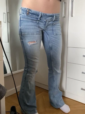 Ljusblåa flare jeans med slitningar - Säljer ett par ljusblåa flare jeans med slitningar och råa detaljer. Jeansen är använda cirka 4ggr dock så är de uppsydda. Tjejen på bilden är cirka 156cm och de är lite korta på mig som är cirka 163.  De skulle nog passa perfekt på någon som är mellan 156-163. Jeansen passar folk som har Xs också