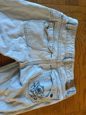 Ljusblå raka jeans med rosbrodyr - Jättesnygga ljusblå jeans med fina, unika detaljer fram och baktill! Säljer då jag inte riktigt fått användning för dem. Midjemåttet är 35 cm och innerbenslängden är 69 cm. 