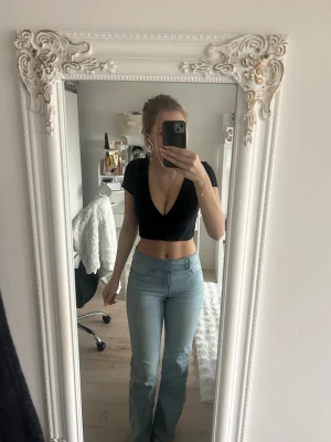 Svart croppad omlottopp från Nelly - Säljer en svart croppad omlottopp från Nelly  med v-ringning och korta ärmar. Perfekt för dig som gillar en stilren och enkel look. Toppens material är mjuk bomull och den har en slim passform som framhäver midjan.