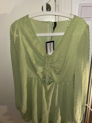 Ljusgrön klänning med snörning - Söt ljusgrön klänning med v-ringning och snörning framtill. Klänningen har långärmade, lätt transparenta ärmar och ett diskret prickigt mönster i tyget. Volang nedtill ger en extra feminin touch. Perfekt för vår och sommar! Kan sänka priset!!