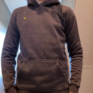 Mörkgrå hoodie från Lyle & Scott - Snygg mörkgrå hoodie från Lyle & Scott med klassisk gul logga på bröstet. Säljer då den inte passar längre. Inga defekter.