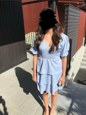 Ljusblå volangklänning med v-ringning - Supersöt ljusblå klänning med v-ringning och trekvartsärm. Klänningen har flera volanglager och en lätt ribbad struktur som ger en extra touch. 