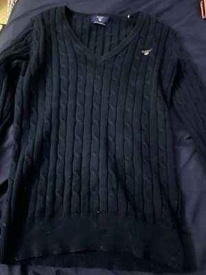 Mörkblå kabelstickad Gant tröja y2k - Svart kabelstickad tröja från GANT i storlek XS. Tröjan har V-ringning, lång ärm och logga , den ger en y2k vibe 