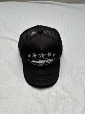 Svart truckerkeps med brodyr - Snygg svart truckerkeps från cortiez med vit brodyr framtill, stjärnor och motiv samt mesh på sidorna och bak. Justerbar passform och klassisk böjd skärm. Perfekt för en streetwear-look.