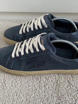 Saint Laurent skor - Snygga blå sneakers i mocka från Saint Laurent med broderad logga på sidan. Skorna har vita snören och beige sula för en clean look. Perfekta för dig som vill ha en stilren och exklusiv sneaker med premiumkänsla. Storlek 40 fit 41