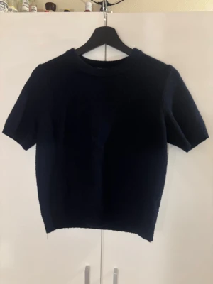 Mörkblå stickad t-shirt från H&M - Säljer en mörkblå stickad t-shirt från H&M med korta ärmar och rund halsringning. Tröjan har en enkel och stilren design, perfekt att matcha med jeans eller kjol. Mjuk och skön stickning. Använt en gång och inte mer då jag inte tyckte den va min stil💕