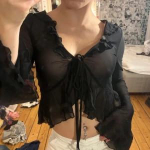 Svart mesh blus med volanger och snörning - Säljer en svart, transparent meshblus med långa ärmar och volangdetaljer längs halsringningen och ärmsluten. från shein och passar xs-m