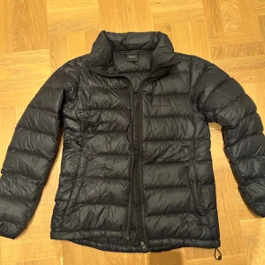 Svart pufferjacka från Peak Performance - Säljer en svart pufferjacka från Peak Performance i storlek M. Jackan har en hög krage, quiltad design och dragkedja framtill. Perfekt för kyliga dagar och enkel att matcha med olika outfits. Klassisk logga broderad på bröstet. Nypris 2300kr