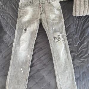 Grå slitna jeans från Dsquared2 - Grå jeans från Dsquared2 med coolt slitna detaljer och hål på benen. Byxorna har färgstänk och en snygg tvättad look. Klassisk femficksmodell med smal passform och låg midja. Perfekta för dig som gillar streetstyle och vill sticka ut.
